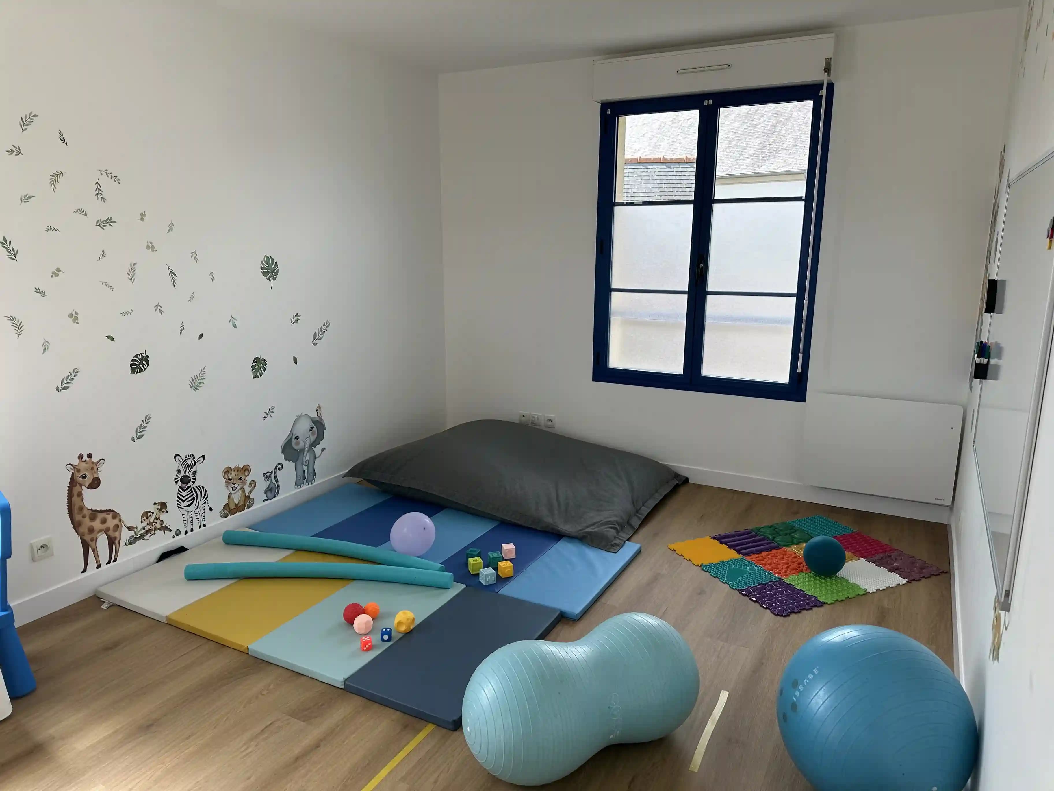 La salle de motricité du cabinet : tapis de sol colorés, ballons et jeux, sous une grande fenêtre